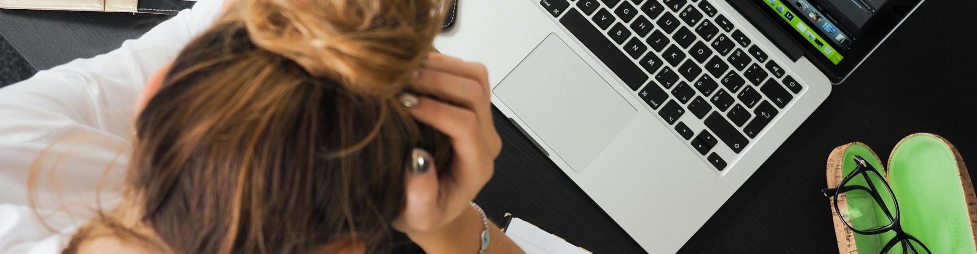 Overhead view of a stressed woman working at a desk with a laptop, phone, and notebooks.